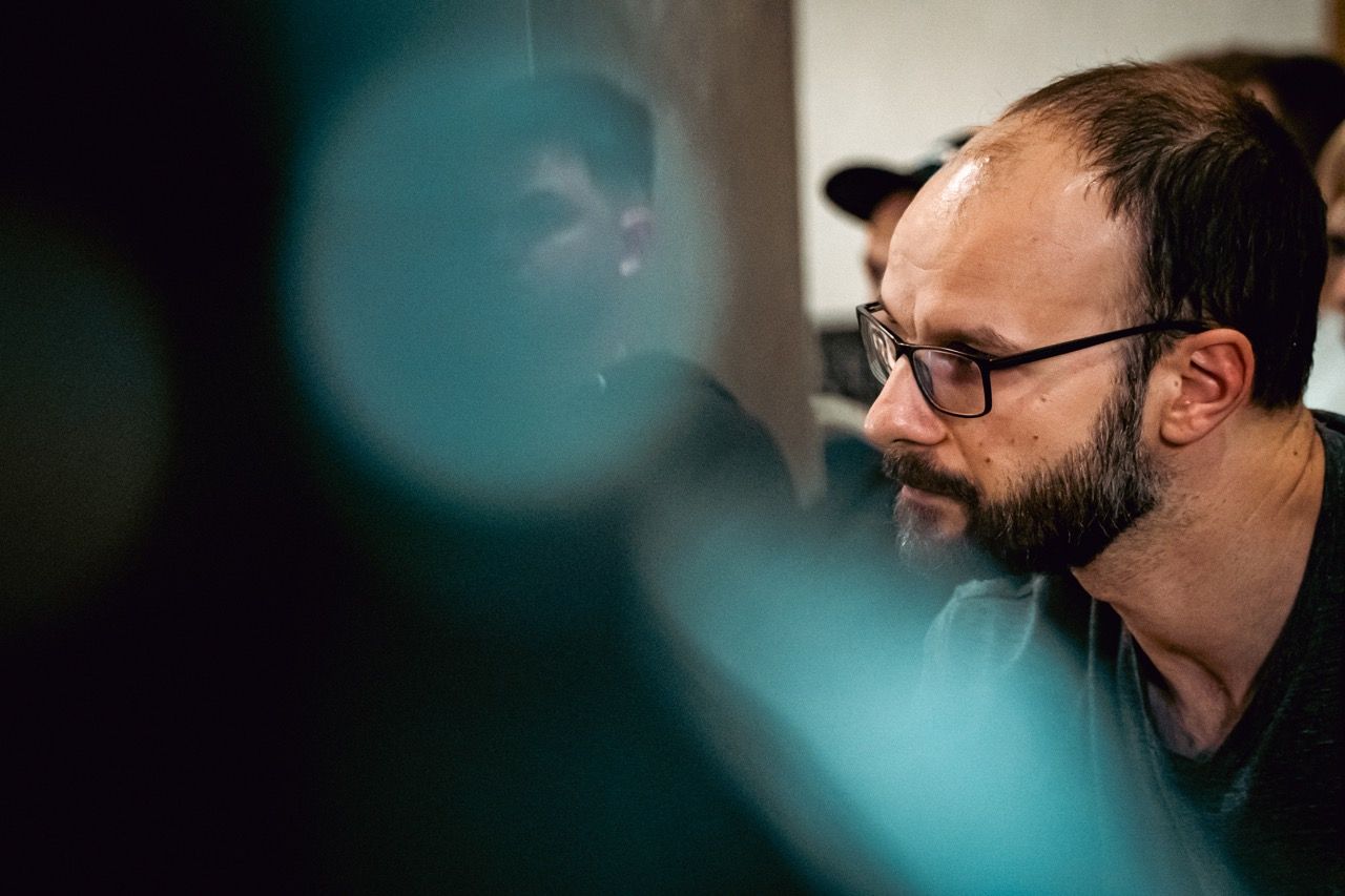 "Man with glasses and a beard, focused, with blurred blue lights."