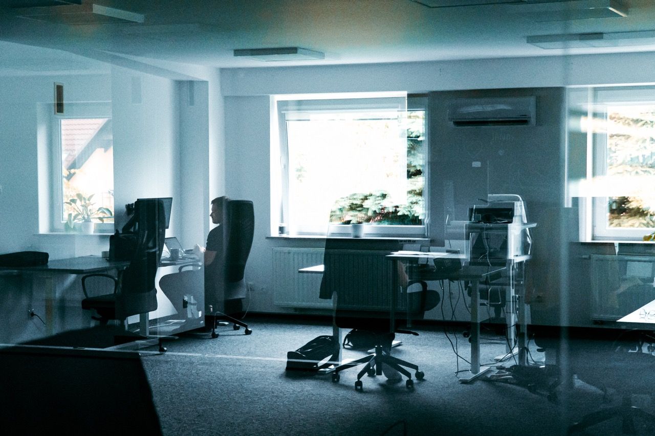 Man alone in a spacious office, viewed through a glass partition with reflections.