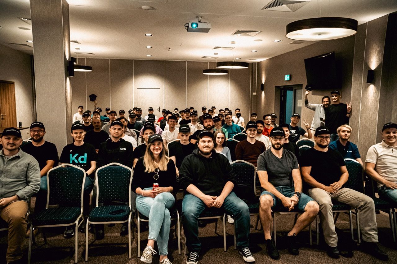 Large group in a conference room, many wearing hats, smiling at the camera.